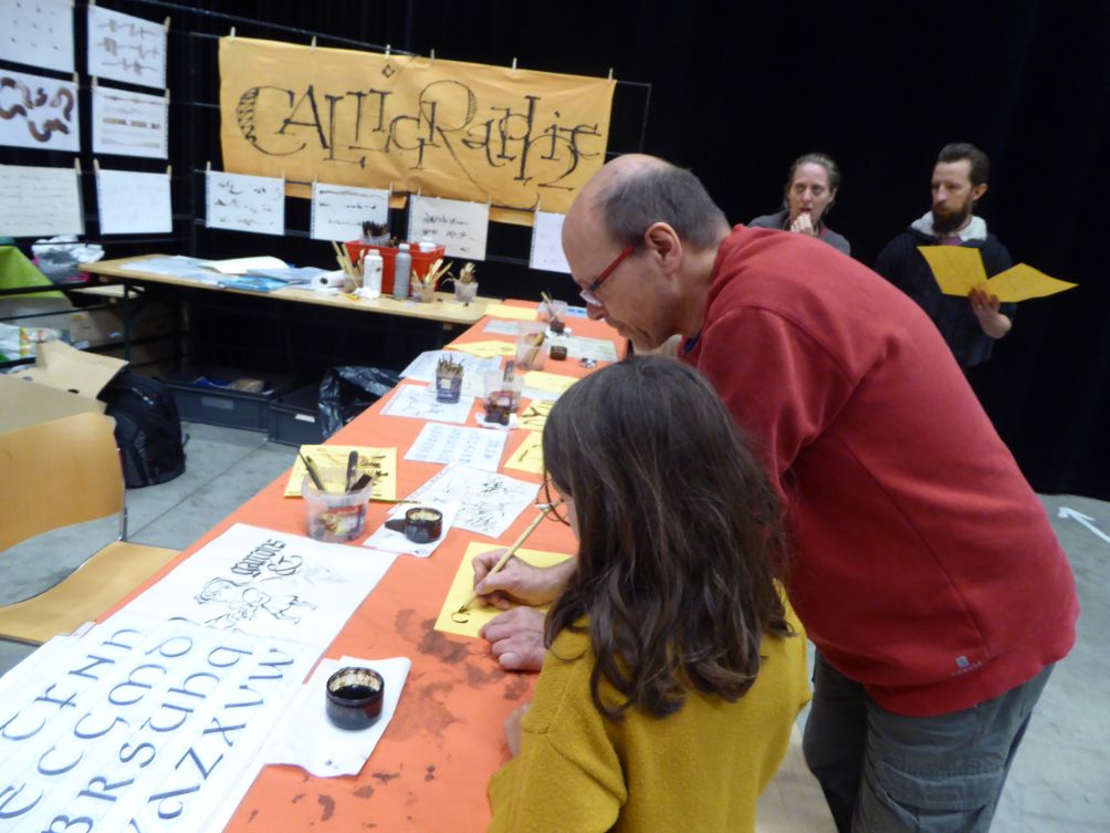 Bruno Riboulot aidant une participante sur son stand de calligraphie